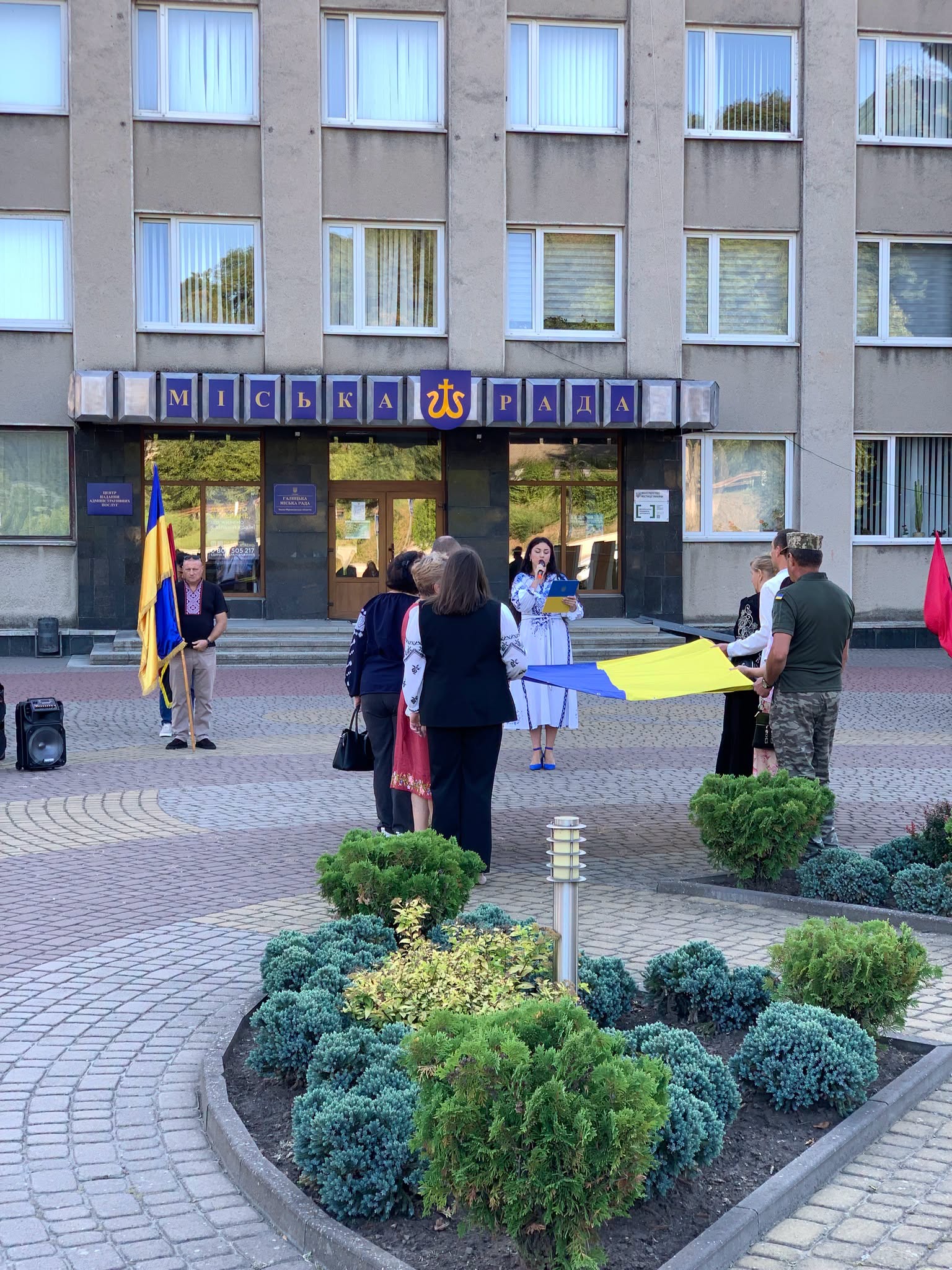 Учасники заходу біля будівлі міської ради з українським прапором.