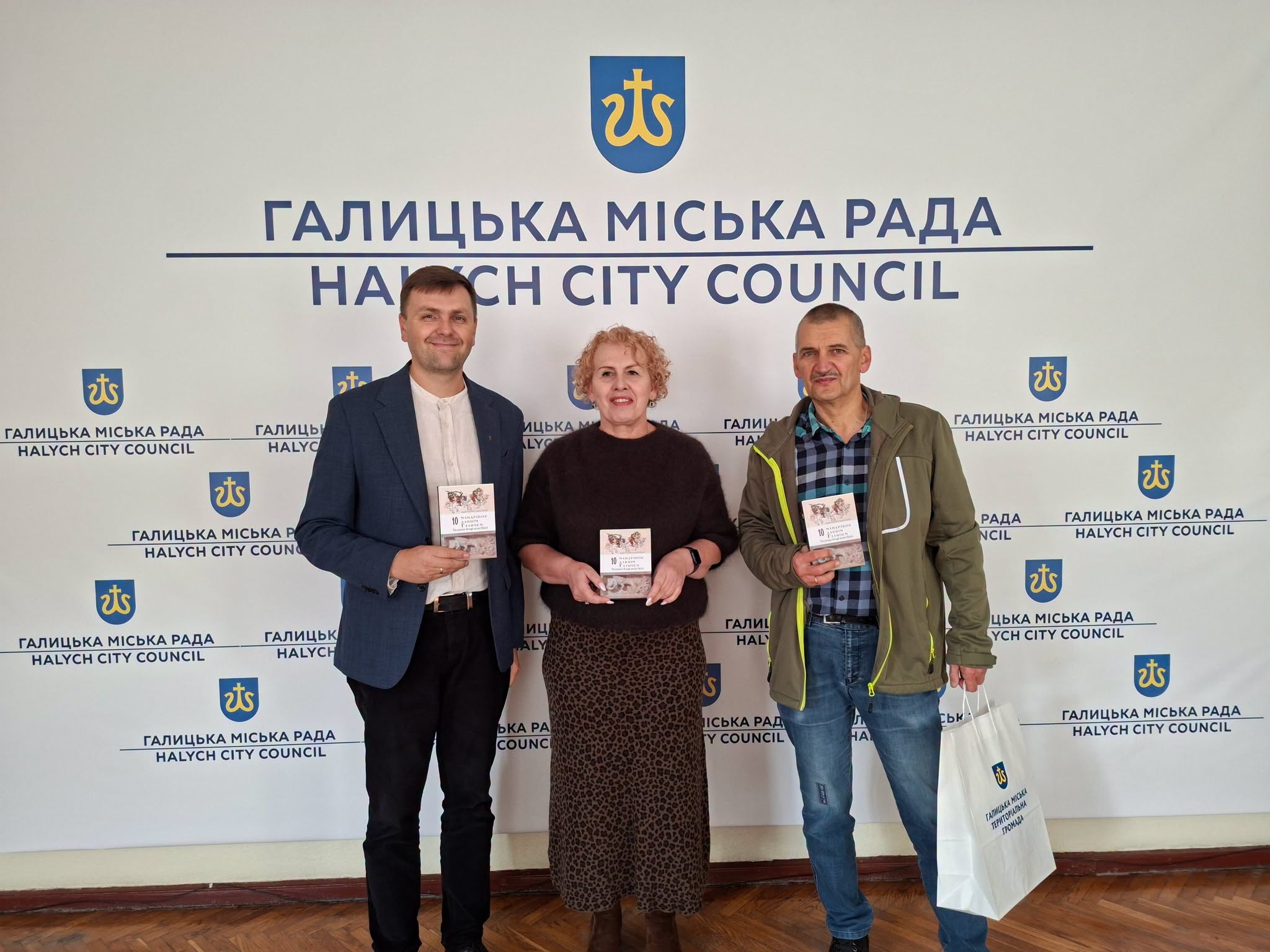 Троє учасників із книгами на тлі банера Галицької міської ради.