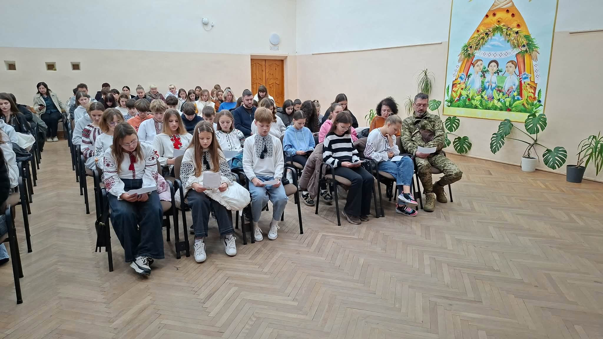 Діти у вишиванках і дорослі читають тексти з аркушів у залі