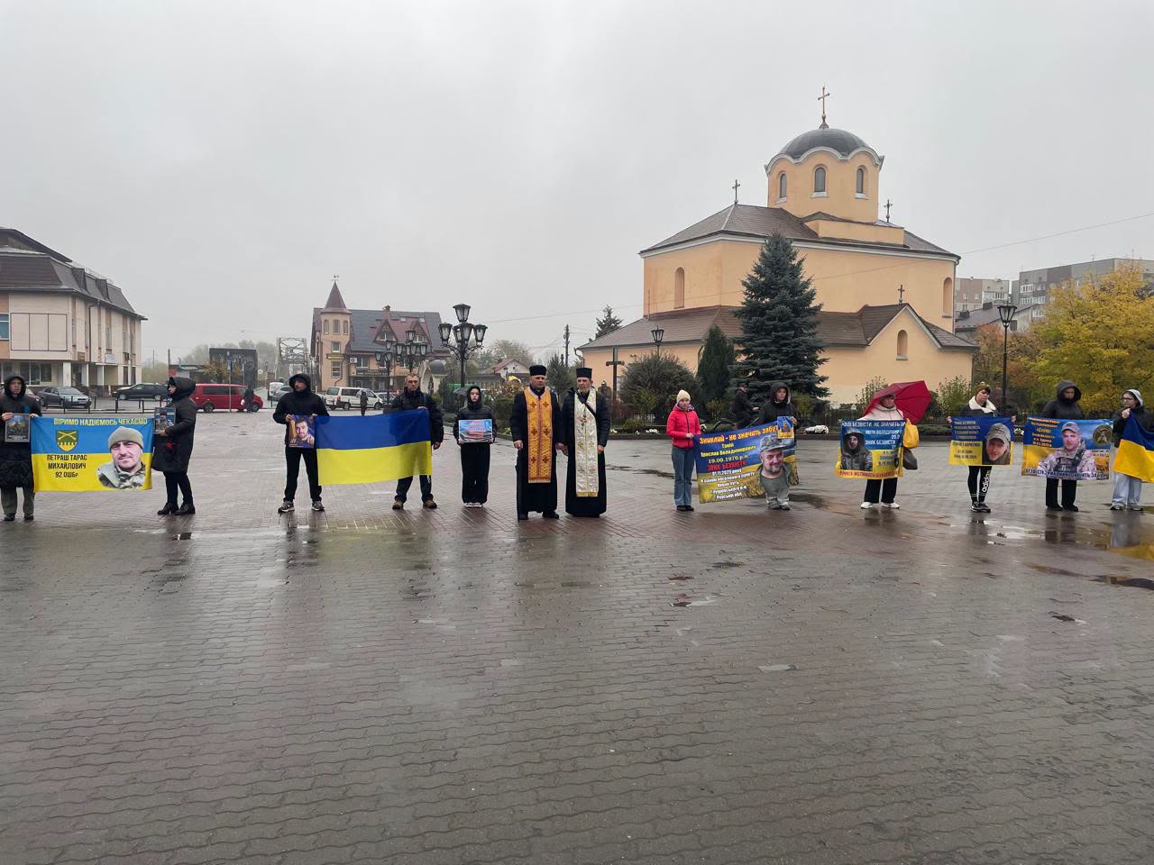 Двоє священнослужителів та учасники акції біля церкви тримають український прапор і плакати про зниклих безвісти військових