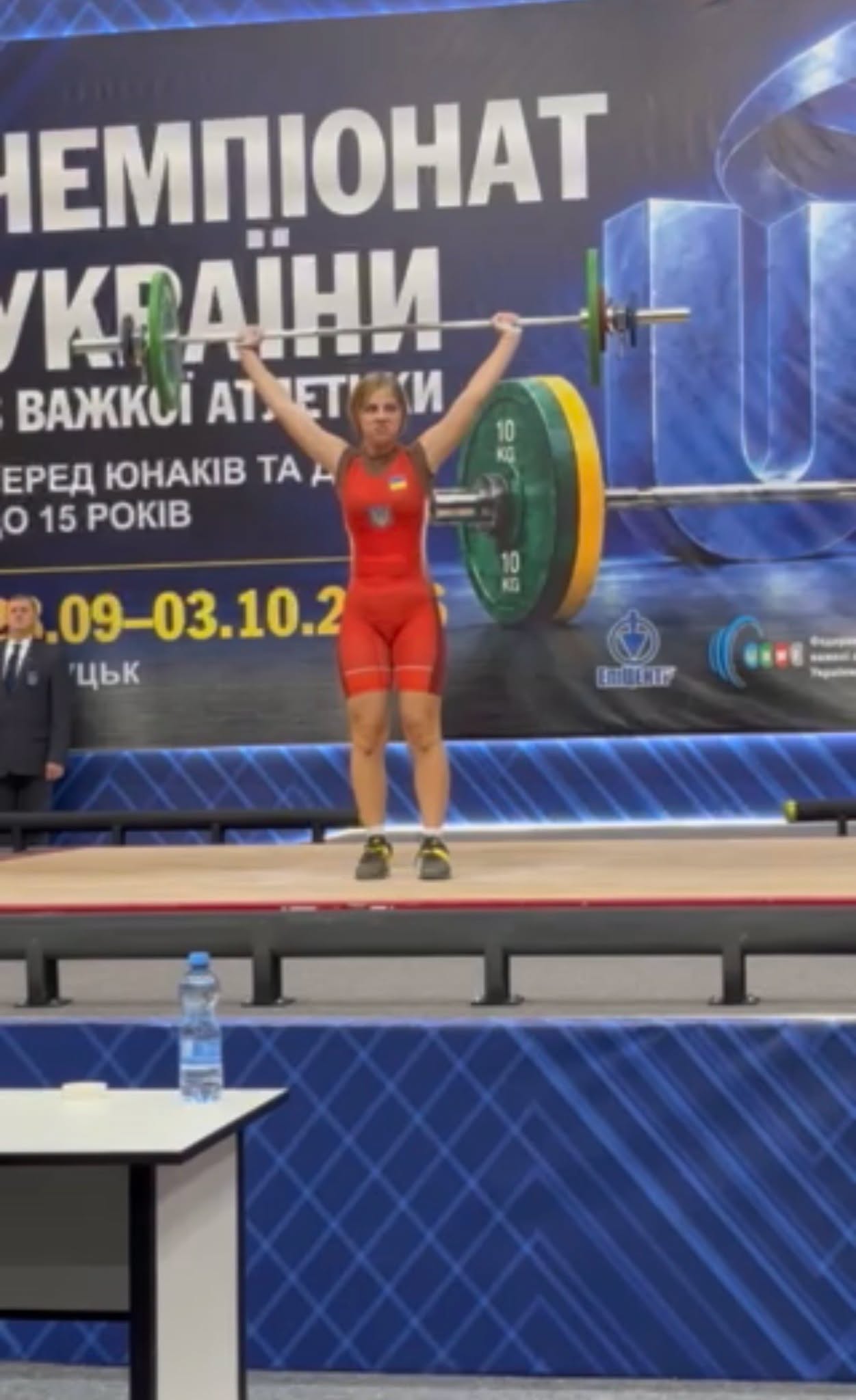 Спортсменка у червоній формі піднімає штангу на чемпіонаті України з важкої атлетики
